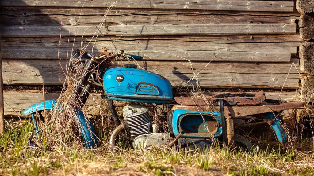 an old motorcycle rusting away next to and old wooden barn