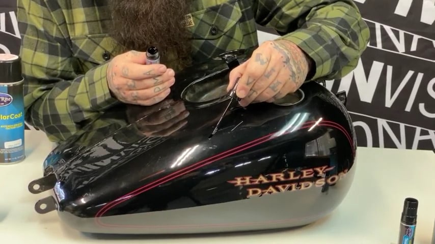 Man applying touch-up paint to motorcycle fuel tank