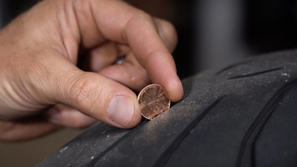 Motorcyclist performing penny test on tire to check tread level