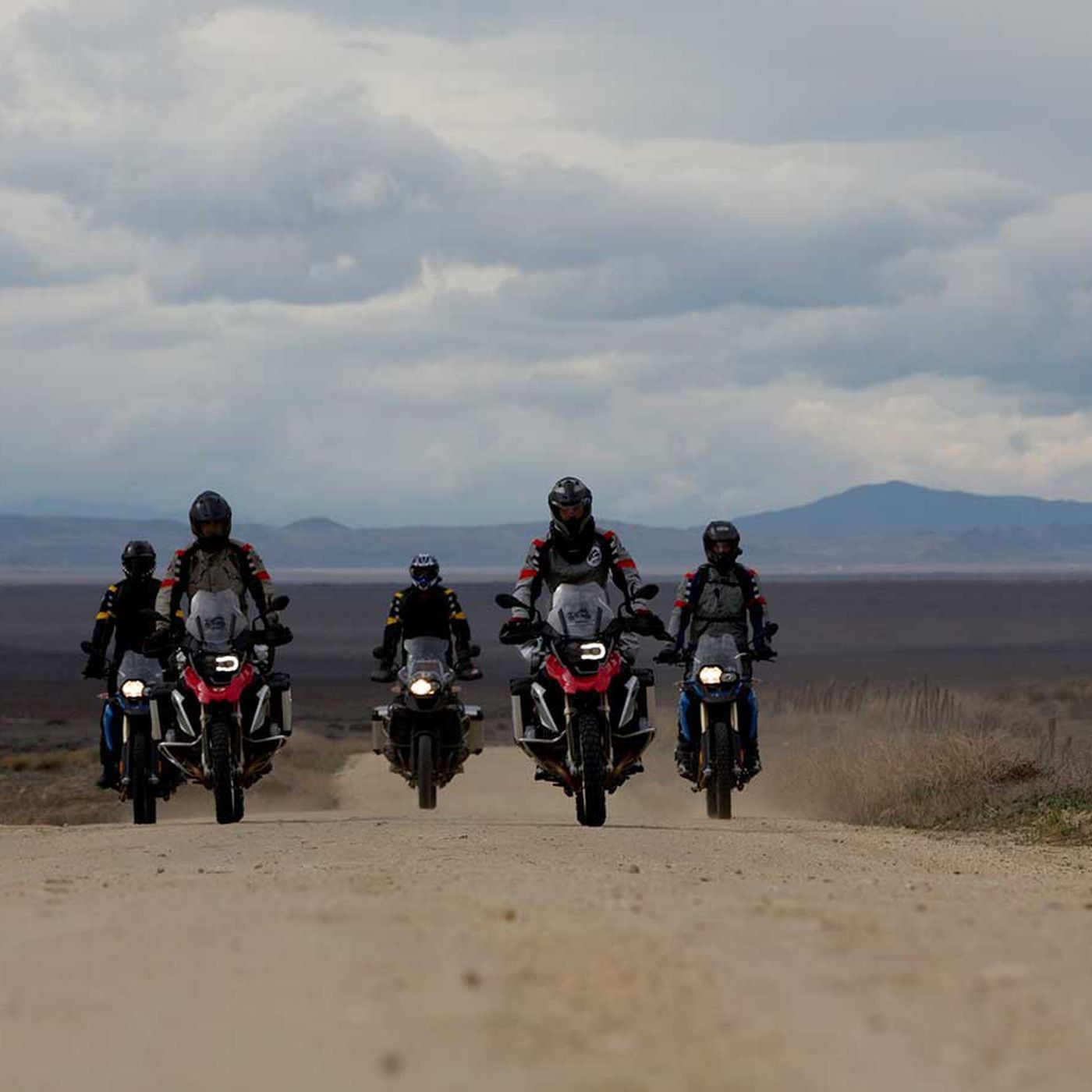 A group of BMW GS motorcycle riders approach the camera on a dirt road