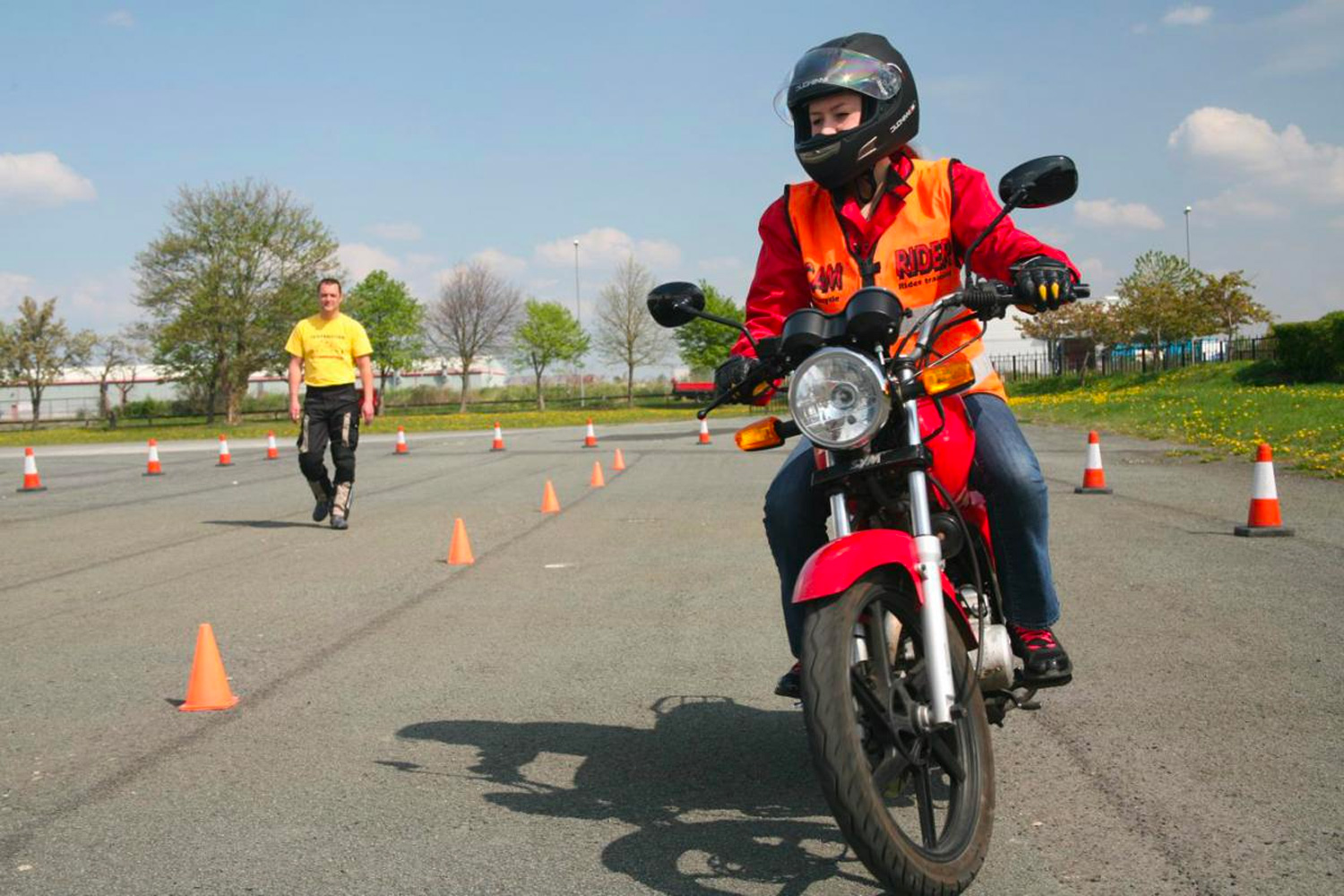 A motorcyclist rides next to a line of pylons in a car park area