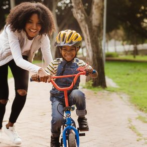 Smiling mother helps young son ride bicycle down pathway during daytime