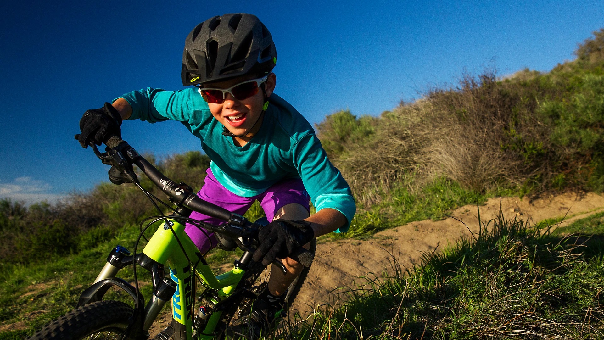 Happy child taking Trek mountain bike down off-road trail during day time
