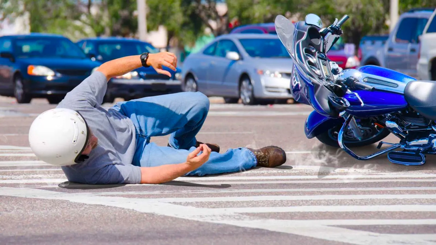 man falls off a motorcycle in an intersection on a busy road
