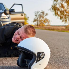 man lies on the road after a motorcycle accident with a car