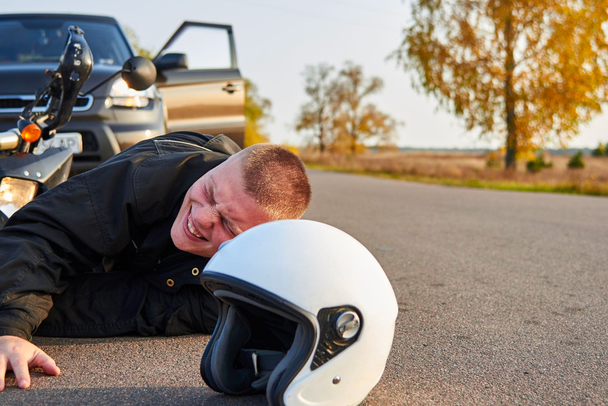 man lies on the road after a motorcycle accident with a car