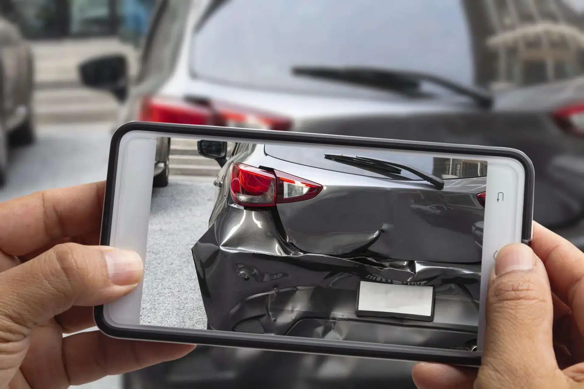 A person photographing damage to a car’s rear bumper with a smartphone.