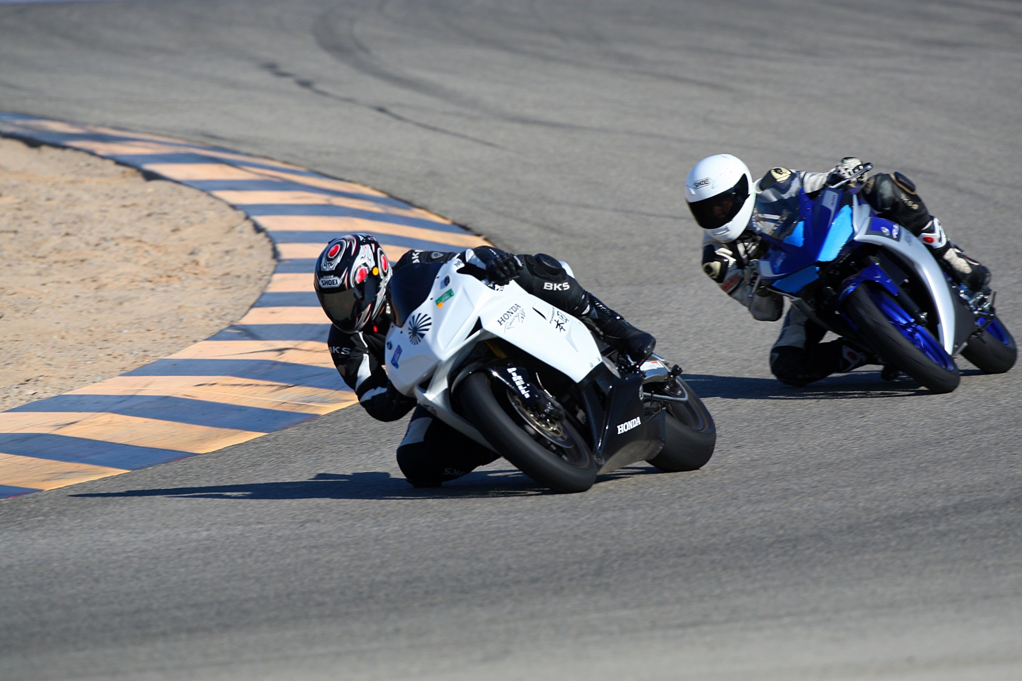 Two riders and their motorcycles at a racetrack