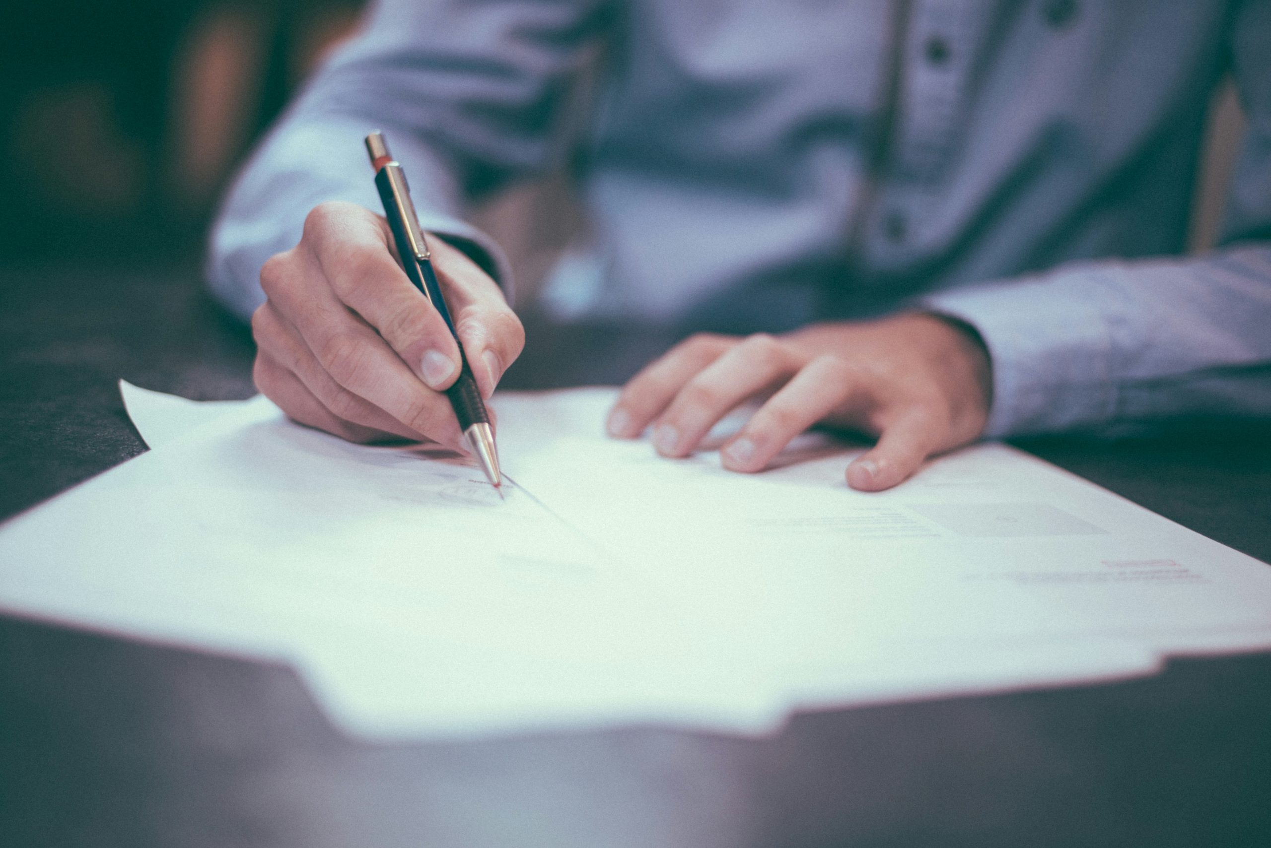 A person signing a document with a pen at a desk.