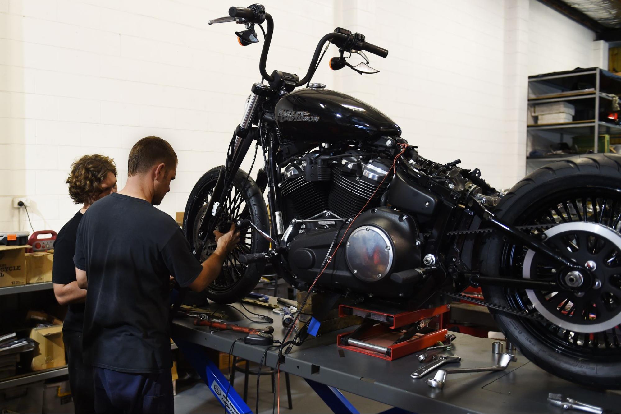 Two mechanics working on a black Harley-Davidson motorcycle
