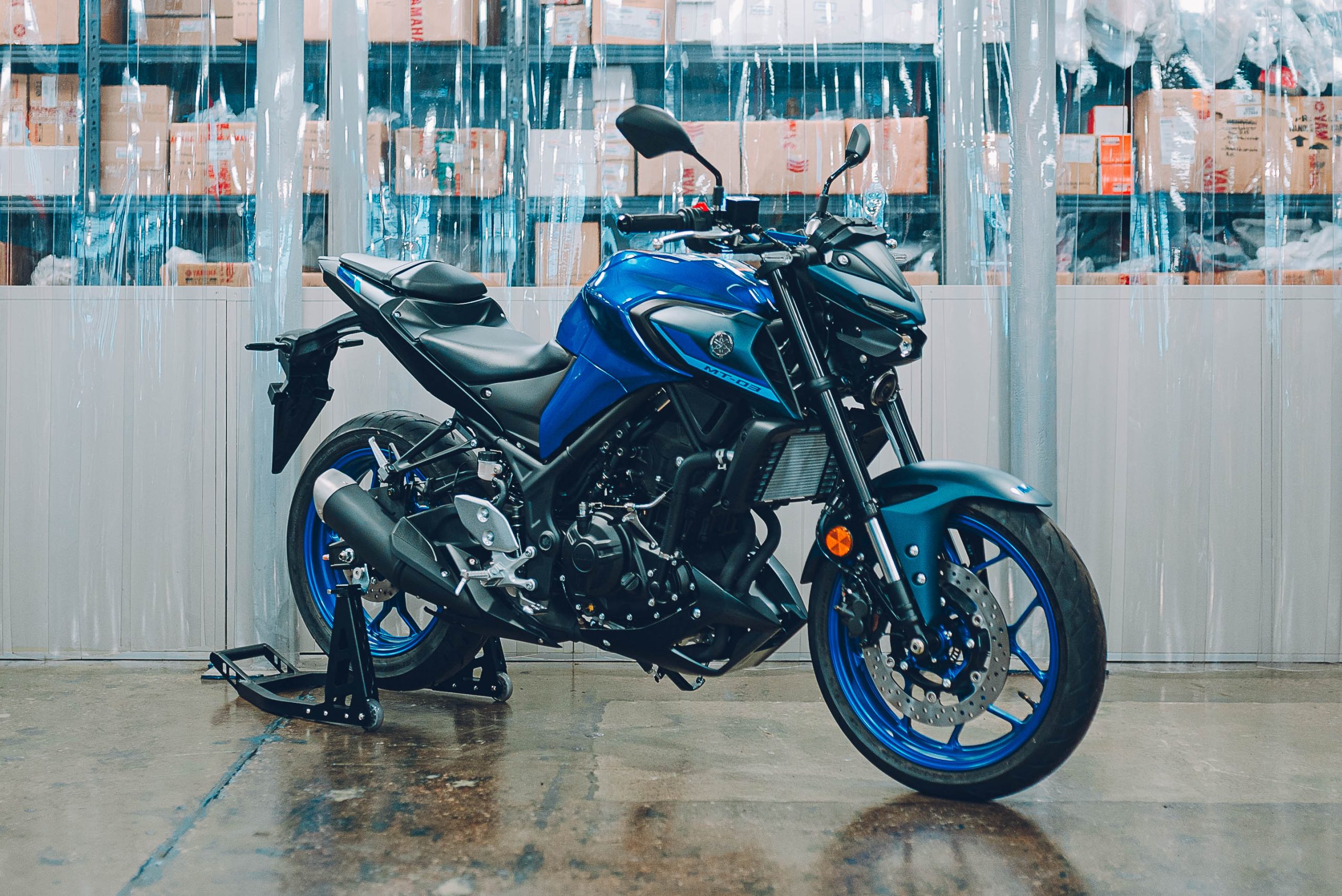 Three-quarter front view of a blue Yamaha MT-03 at a warehouse