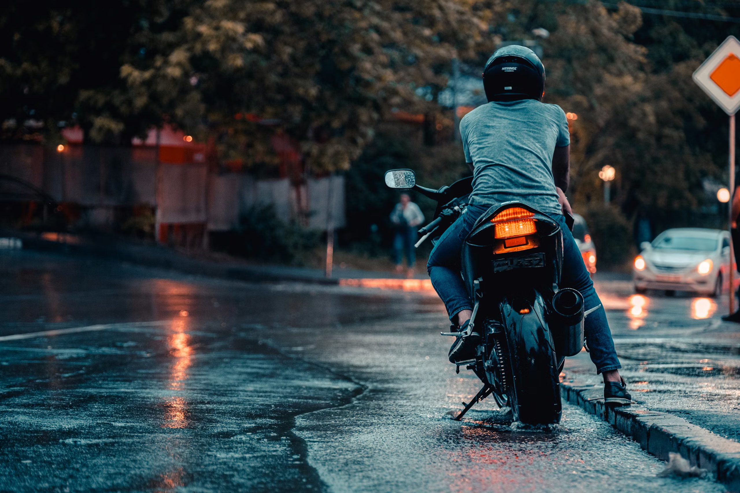 Motorcyclist stopped at a wet intersection during rainy conditions.