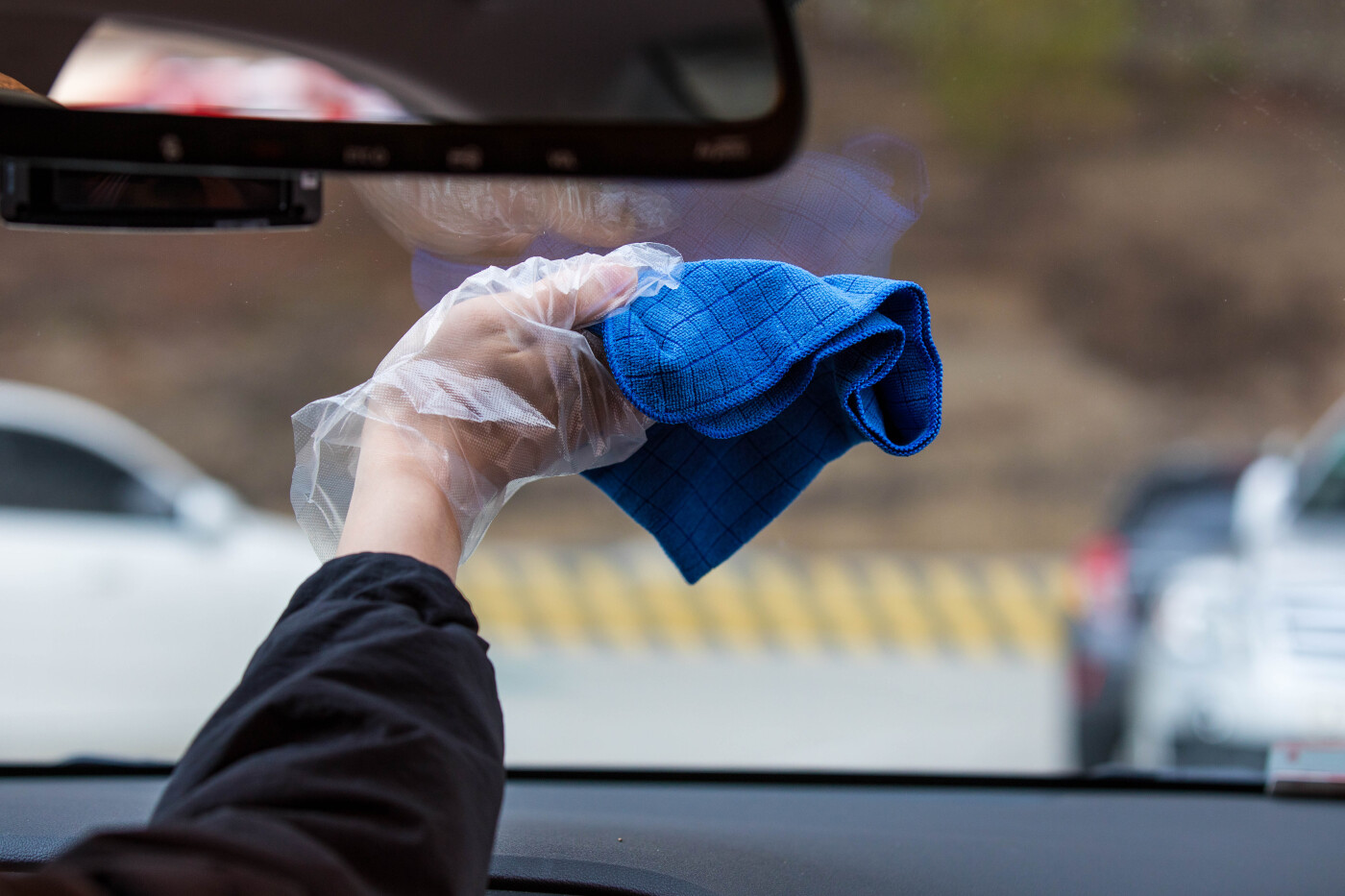 Hand holding a blue fiber towel to wipe the car window. Cleaning car's windshield with microfiber cloth from the inside.